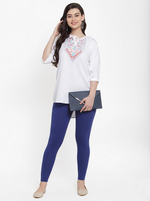 Women wearing blue cotton lycra leggings styled with a white embroidered tunic, paired with beige flats and a navy clutch for a casual look.